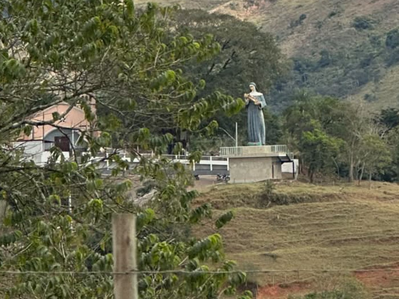 Estátua de santa branca ao lado de uma igreja no alto de um morro
