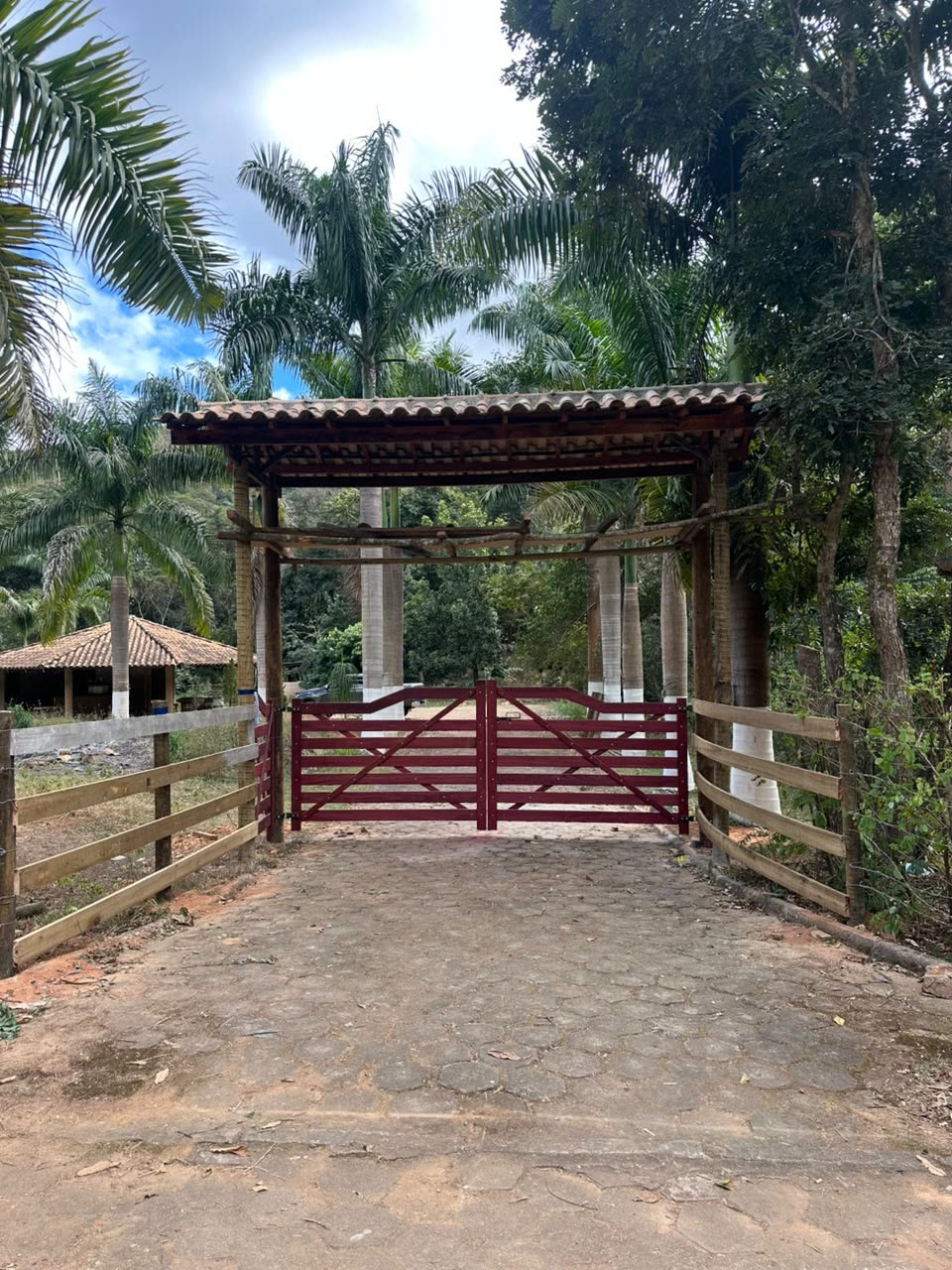 Portal de madeira com portão vermelho na entrada do sítio